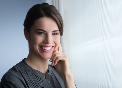 Young attractive woman smiling next to the window and looking at camera.