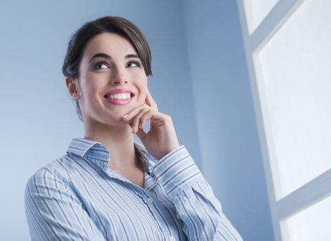 Young attractive woman smiling in front of the window and touching her chin.