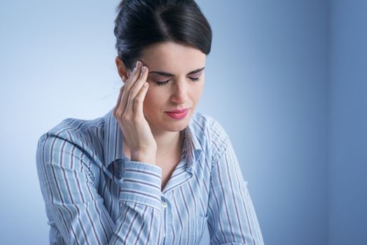 Young woman with headache touching her temples.
