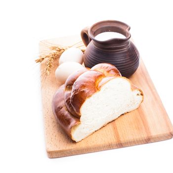 Fresh loaf of challah with milk and eggs on the wooden board