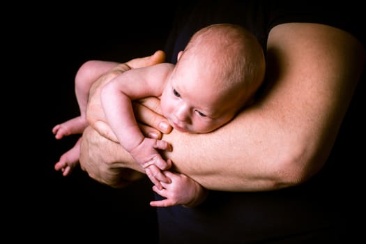 Newborn baby on the father's hands on black