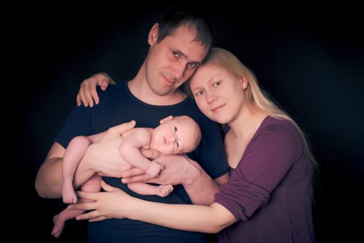 Newborn baby on the father's hands and mother on black