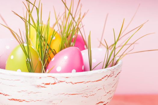 Decorative eggs in pot with grass over pink background. Easter decor.