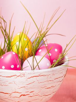 Decorative eggs in pot with grass over pink background. Easter decor.