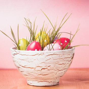 Decorative eggs in pot with grass over pink background. Easter decor.