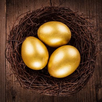 golden eggs in the nest over wooden background with copy text