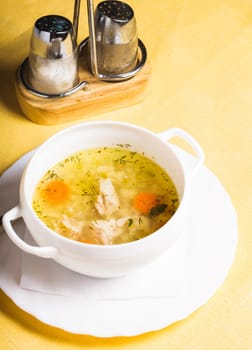 A chicken broth in white ware on the yellow tablecloth