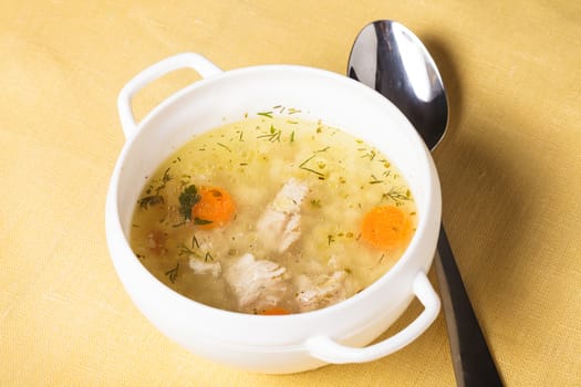 A chicken broth in white ware on the yellow tablecloth
