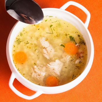 A chicken broth in white ware on the orange tablecloth