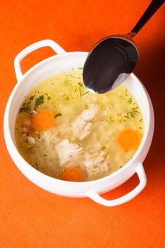 A chicken broth in white ware on the orange tablecloth