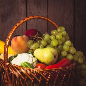 Basket of vegetables and fruits over wooden background