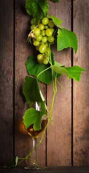 Grapes with leaves and glass of wine on the wood background