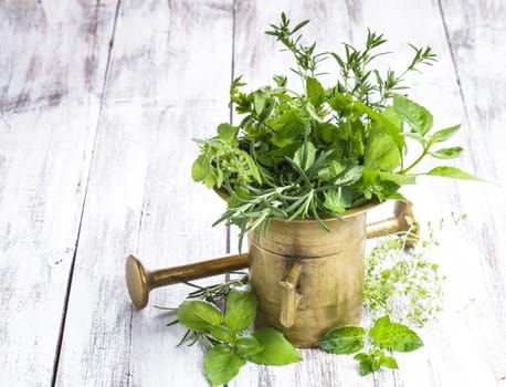 Fresh herbs in the copper mortar on the shabby wooden table