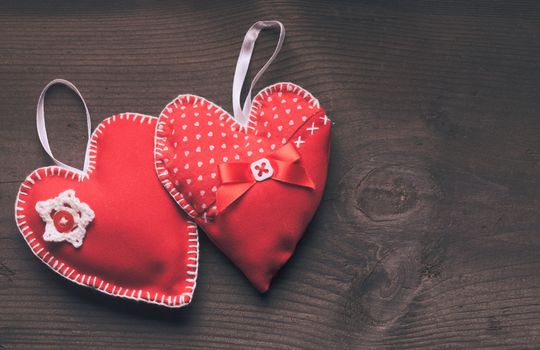 Sewed two handmade red hearts on wooden background