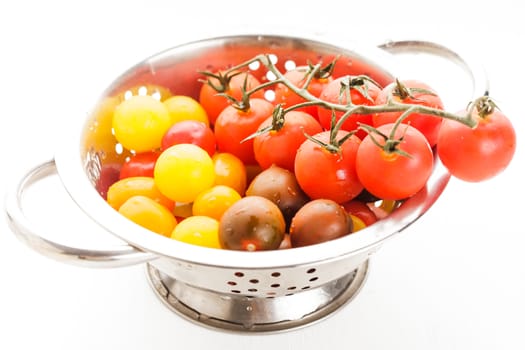 Red, yellow and black  cherry tomatoes in colander on white