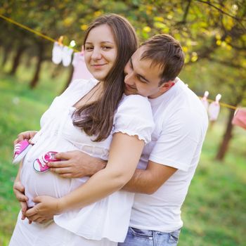 Pregnant couple outdoor in the garden, hold the baby booties