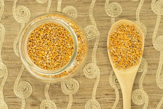 Bee pollen in glass pot and wooden spoon on beige background fabric