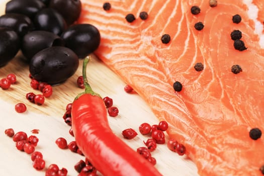 Salmon fillet with olives and red pepper. On a wooden plate.