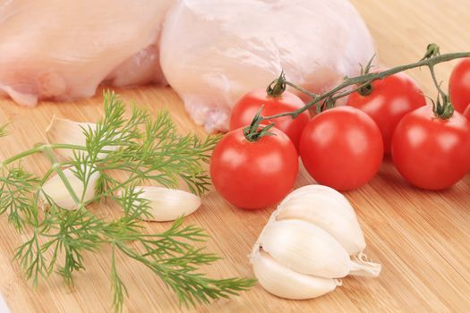 close up of raw chicken breast with vegetables on wooden platter