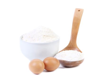 Spoon and bowl with flour two eggs. Isolated on a white background.