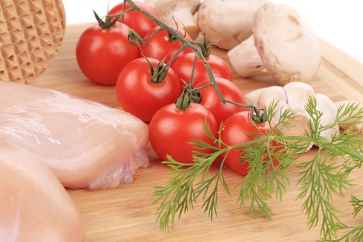 close up of raw chicken breast with vegetables on wooden platter