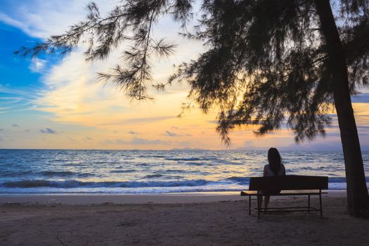 woman sit on chairs under tree on beach at sunset