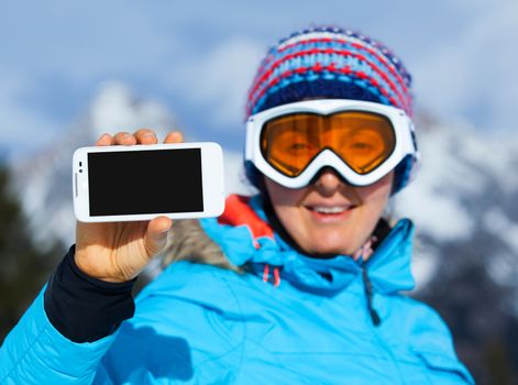 Young Skier woman showing display of mobile cell phone with black screen and smiling