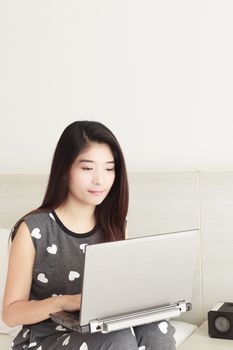 Young Asian woman playing internet on notebook and smiling