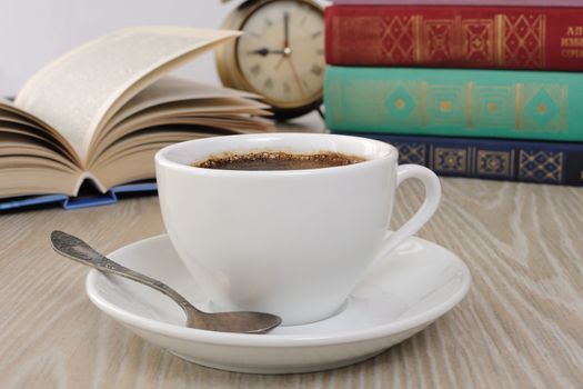 A cup of fragrant black coffee on the table against the background of an open book

