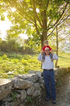 Happiness grandfather holding grandchild on his shoulders in front of a tree