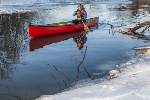 a senior male paddling a red canoe in winter - Cache la Poudre River in Fort Collins, Colorado