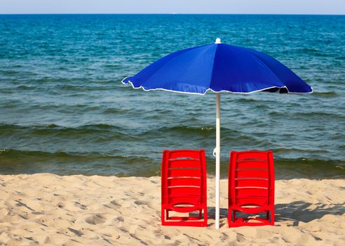 Two red plastic chairs with umbrella on a beach