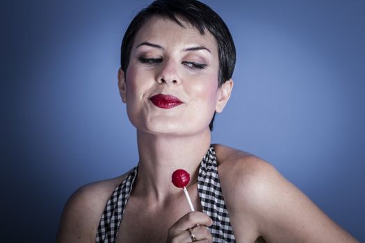 Sexy happy young woman with lollypop in her mouth on blue background