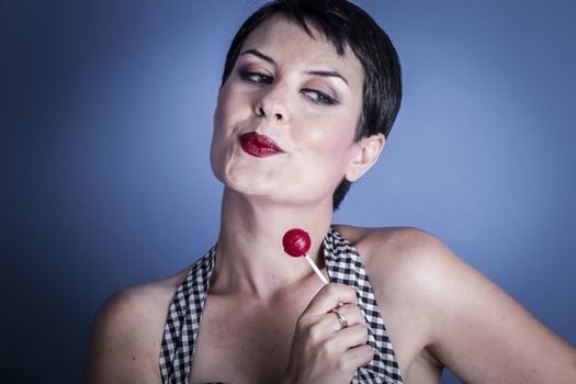 Sexy happy young woman with lollypop in her mouth on blue background