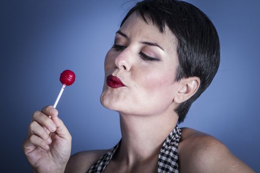 Candy, happy young woman with lollypop in her mouth on blue background