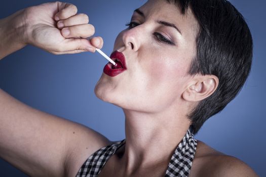 happy young woman with lollypop in her mouth on blue background