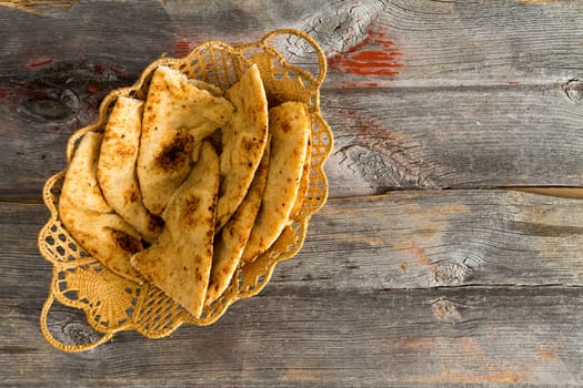 Delicious crusty whole grain naan flatbread slices, a leavened bread cooked in a tandoor clay oven, served in a decorative wicker basket on rustic weathered wooden boards, overhead view