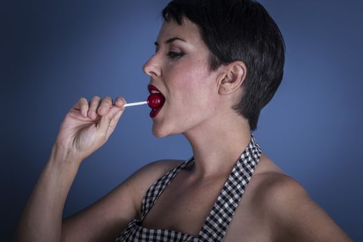 Lolly, happy young woman with lollypop in her mouth on blue background