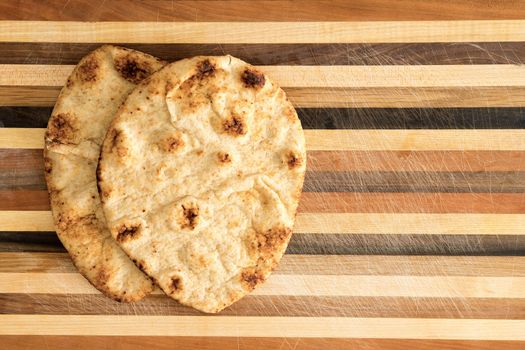 Crisp crusty naan whole grain flatbread that has been cooked in a traditional Indian tandoor clay oven served on a decorative striped wooden surface with copyspace