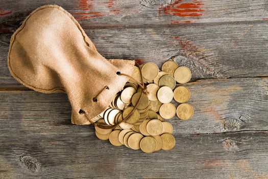 Pile of dollar coins spilling out of a drawstring pouch onto a rustic old weathered wooden table, view from above with copyspace