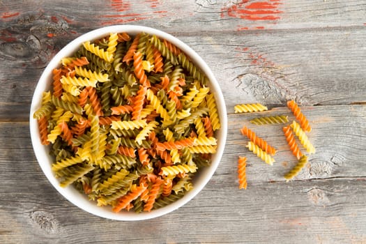 Colourful bowl of uncooked tomato and spinach fusilli pasta, a traditional Italian pasta made from spirals and corkscrews of dried durum wheat dough, on a rustic wooden background with copyspace