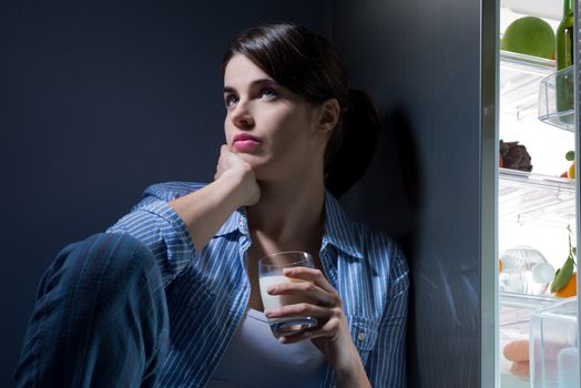 Sleepless sad woman sitting on kitchen floor having a glass of milk.