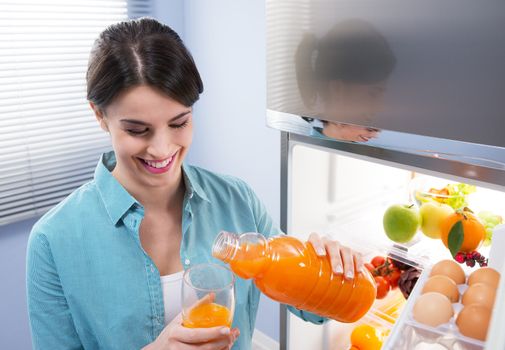 Cheerful young woman pouring fresh fruit juice into a glass.