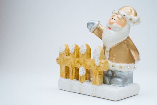 Golden old time Santa Claus figurine standing behind garden fence and waving with one hand, shot in studio with light background