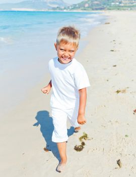 Smiling cute boy runs along the tropical beach.