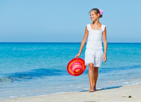 Relaxing beach girl walking with a sun hat at the beach.