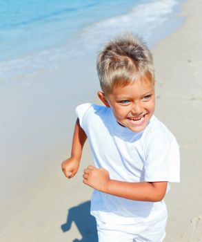 Smiling cute boy runs along the tropical beach.