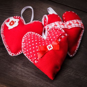 Sewed handmade red hearts on wooden background