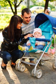 Happy family outdoor - mother, father and daughter in baby carriage