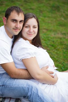 Pregnant couple are sitting on the grass in the park